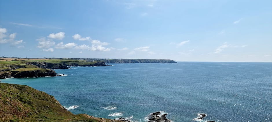 Panoramic view of Cornwall's rugged coastline meeting the blue sea on a clear summer's day